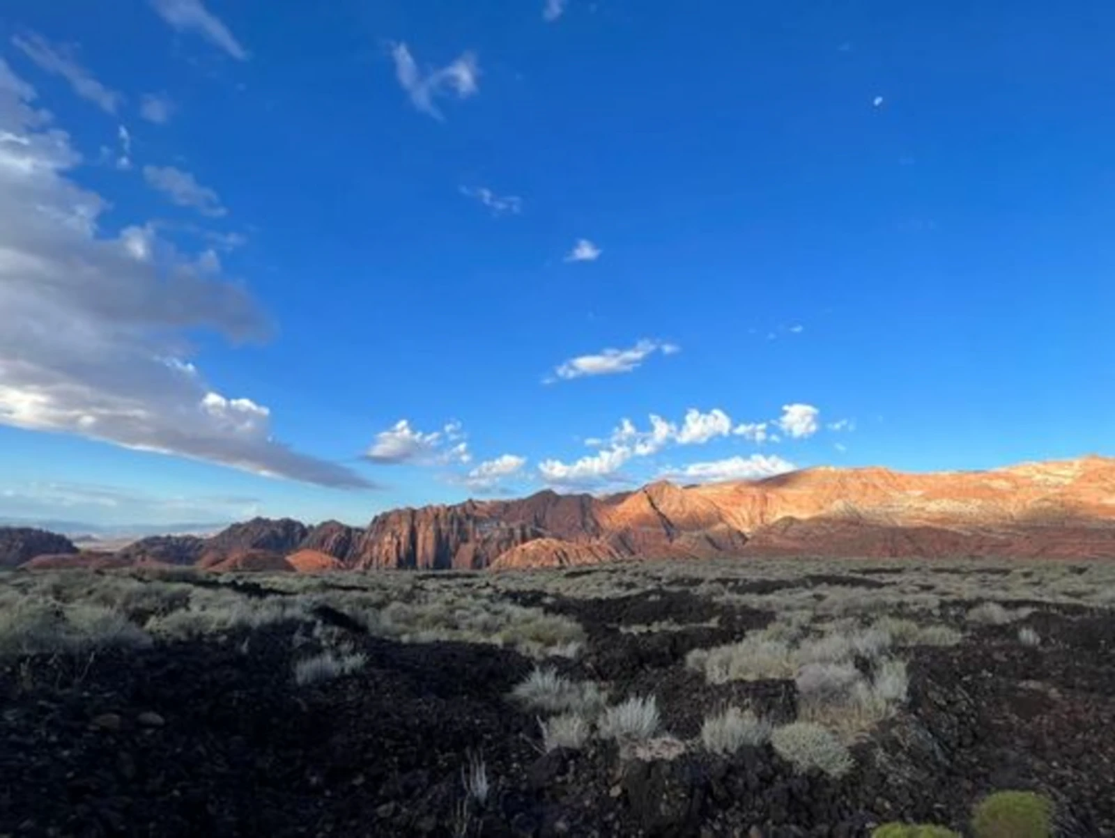 Black lava field and red rock cliffs under a blue sky in St. George, Utah
